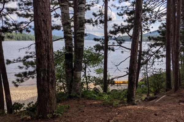 campsite looking through trees at lake with canoe on sandy beach