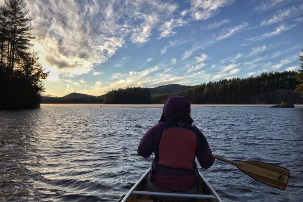 Paddling in a canoe on lake with sunset in the distance.